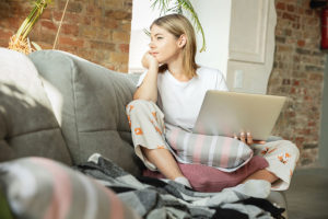 woman gazing out into the distance while sitting on a couch with a laptop on her lap